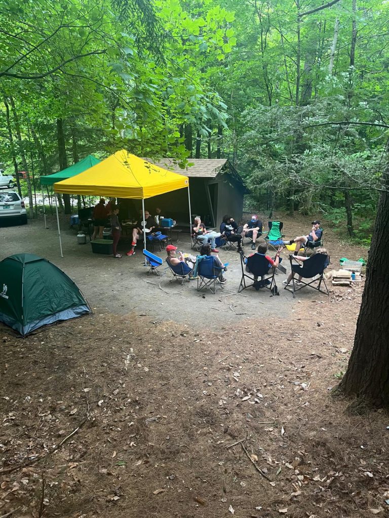 A campsite with tents and people gathered around a table under yellow canopy.