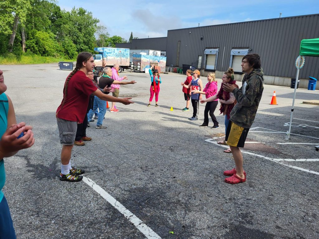 Children play with a ball near an adult and buildings in background.