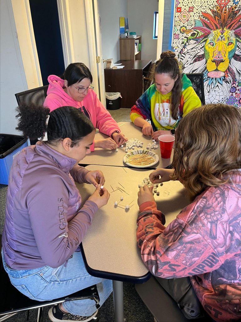 Four girls sitting at a table with plates and food while playing with toys.