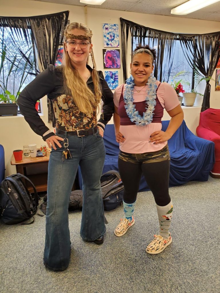 Two girls with leis stand before a room filled with art and furniture.