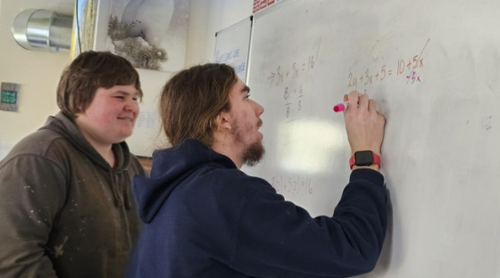Two men writing with markers on a whiteboard.