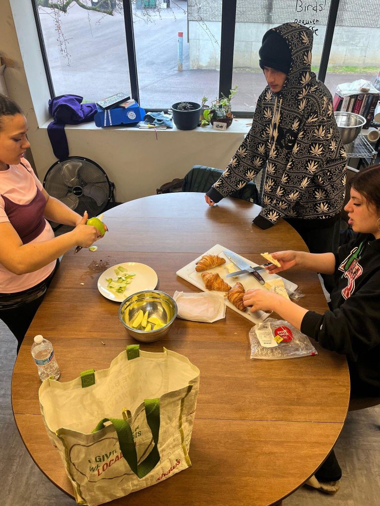 Three people sitting at a table with food and drinks while wearing hooded sweatshirts.