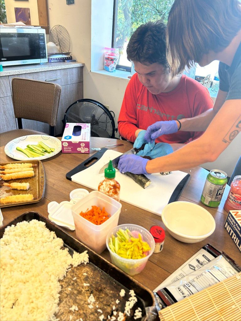 Two people are preparing food at a table with various ingredients and utensils.
