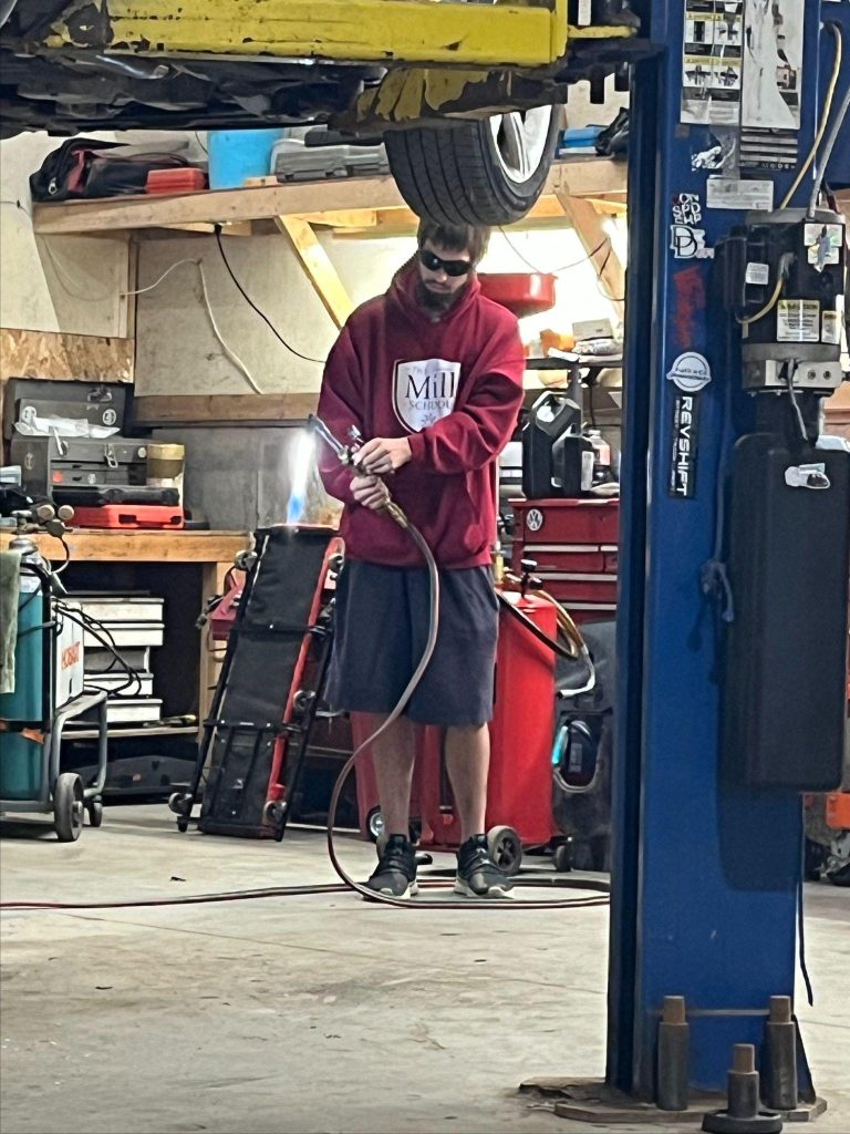 A person is welding a tire to a car at an auto shop with various tools and equipment around them.