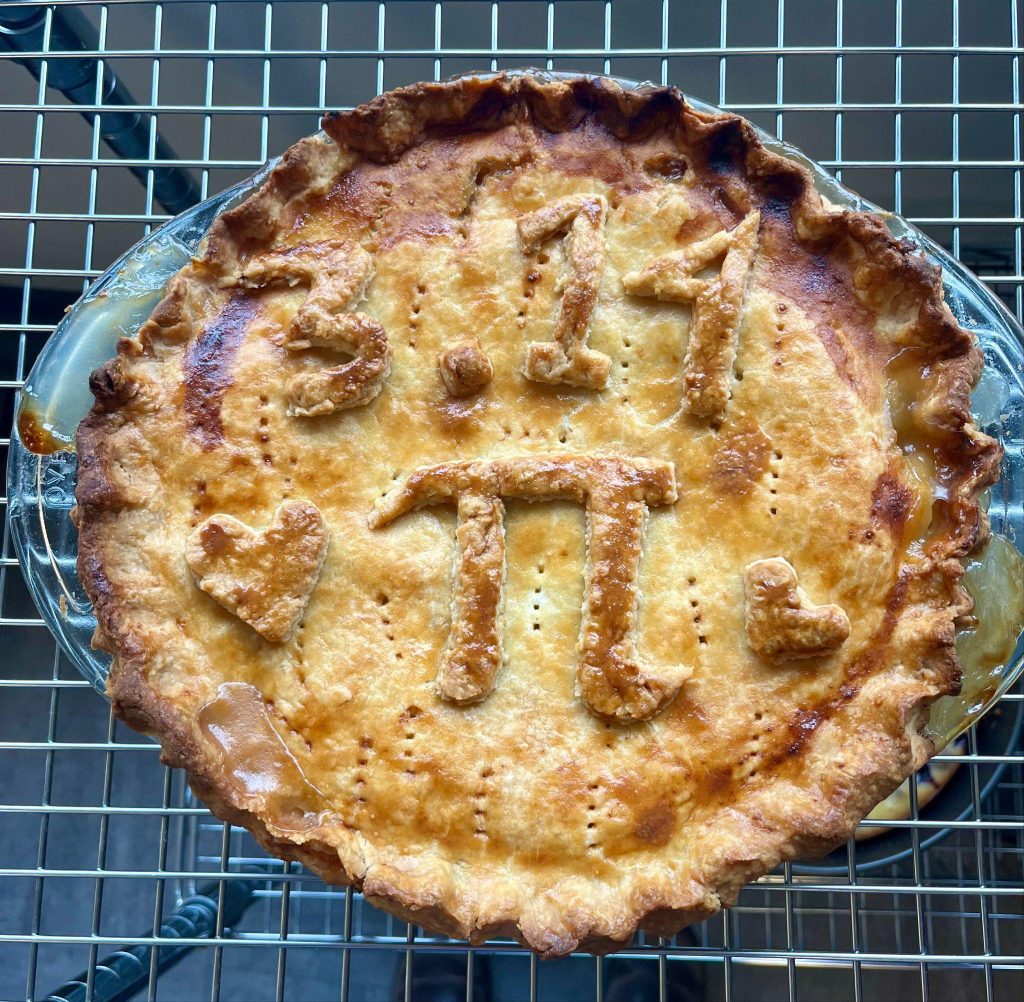 A baked pie with a design resembling pi symbols is placed on a wire rack.